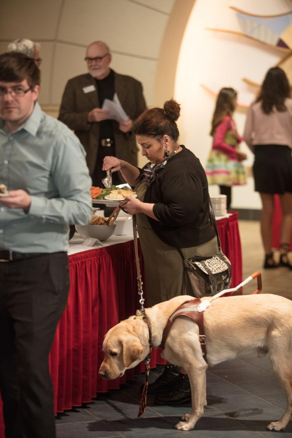 A woman and her service dog getting food at the buffet table
